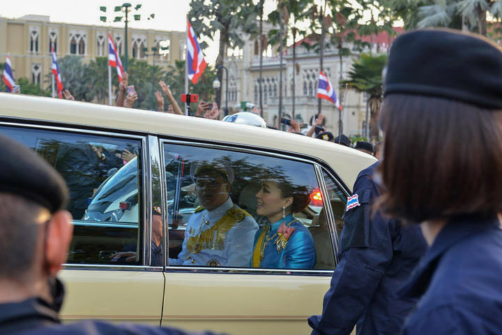 Thailand's Queen Suthida and Prince Dipangkorn Rasmijoti are driven in a motorcade past a pro-democracy rally, as anti-government protesters (back) hold up their three-finger salute, in Bangkok on October 14, 2020. 