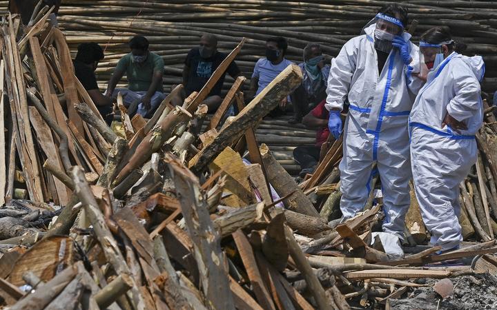 Family members and relatives wearing PPE perform the last rites amid the funeral pyres of Covid-19 victims during a mass cremation held at a crematorium in New Delhi on April 27, 2021. 