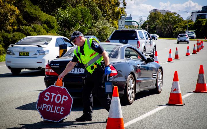 A Queensland police officer moves a stop sign at a vehicle checkpoint on the Pacific Highway on the Queensland - New South Wales border, in Brisbane on April 15, 2020. 