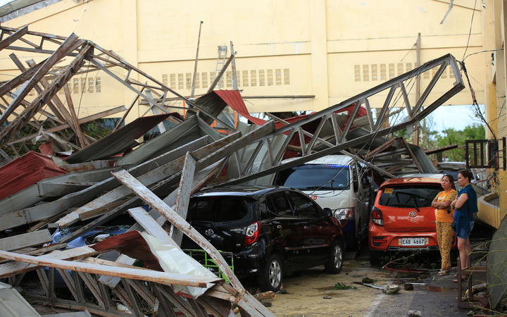 Residents stand next to cars damaged after a gymnasium collapsed at the height of super Typhoon Goni after it hit Tabaco, Albay province, south of Manila on November 1, 2020. 