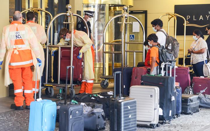 Local officials in protective gear help with baggage as Australian residents arrive at a hotel in Adelaide for mandatory 14-day quarantine after returning on a repatriation flight on 21 April 2020. 