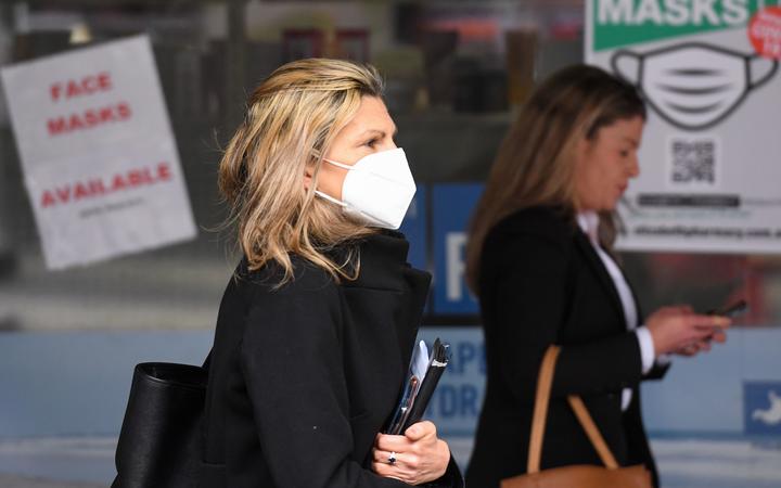 People wearing face masks walk past a sign advertising masks in Melbourne on July 20, 2020.