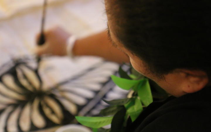 Steady hands  in the final stages of Tongan ngatu making, adorning the ngatu with intricate Tongan symbols and designs.