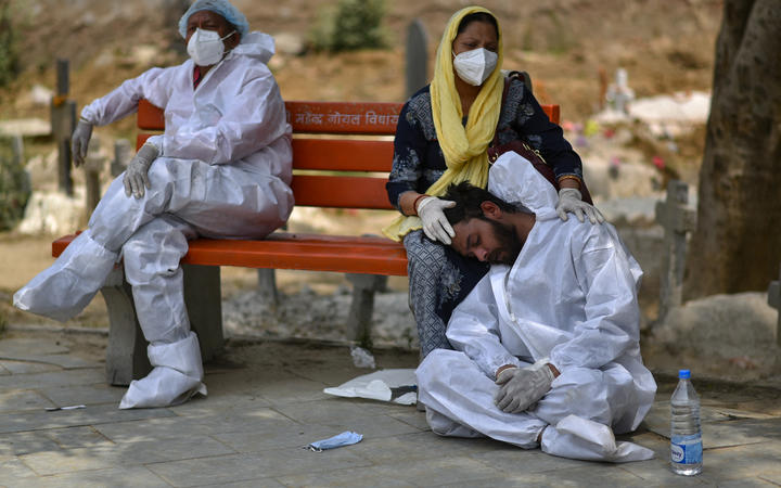 An exhausted health worker wearing personal protective equipment rests at a bench at a graveyard, in Delhi, India