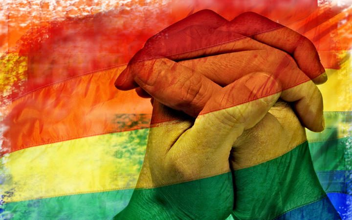 double exposure of a rainbow flag and the hands of a young man put together like praying