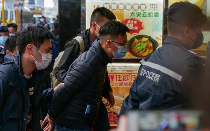 Stand News chief editor Patrick Lam (C) is brought to the news outlet's office building in handcuffs after police were deployed to search the premises in Hong Kong's Kwun Tong district on 29 December 2021.