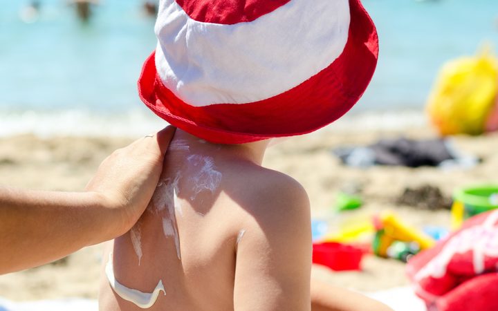 Child on the beach putting sunscreen.