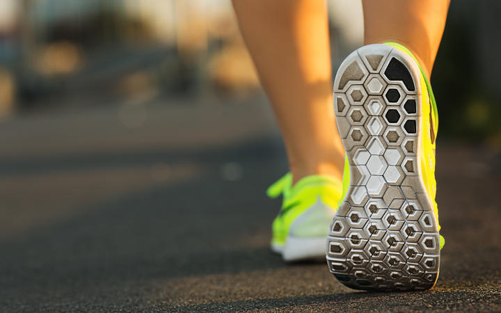 Woman runner showing feet and running shoes on track or road.